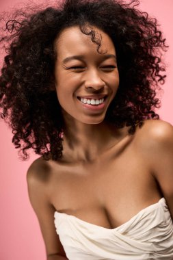 Kıvırcık saçlı güzel bir kadın ışıl ışıl gülüyor, mutluluk ve pozitiflik saçıyor..