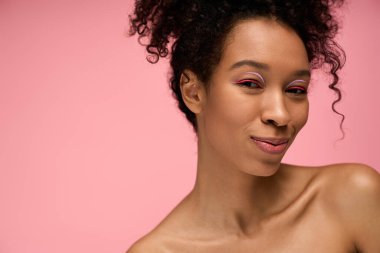 Kıvırcık saçlı güzel bir kadın pembeye karşı canlı bir portrede cazibe ve neşe saçar..