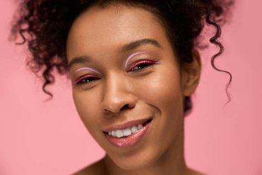 Kıvırcık saçlı genç kadın renkli makyajını sergilerken saf neşe ve mutluluğu ifade ediyor..