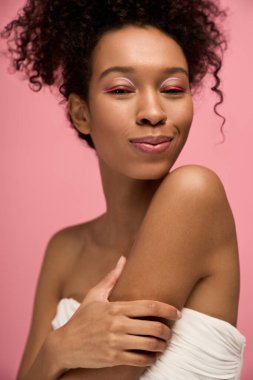 Pembeyle çevrili anı kucaklayan kıvırcık saçlı genç bir kadının neşeli ifadesi..