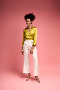 Neşeli genç bir kadın parlak sarı bir gömlek ve beyaz pantolon giyer, neşe ve güven saçar..