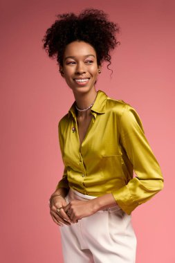 Genç bir kadın, stüdyoda zarif bir şekilde tasarlanmış açık sarı bir gömlek giyerek mutluluk saçar..