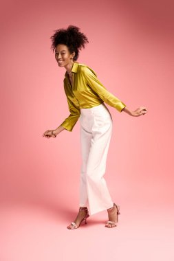 Genç, güzel bir kadın, şık sarı bir bluz ve beyaz bir pantolonla dans ederken mutluluğunu ifade eder..