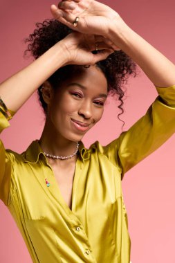 Kıvırcık saçlı genç bir kadın şık yeşil bir gömlek giyerken neşe ve zarafet taşıyor..