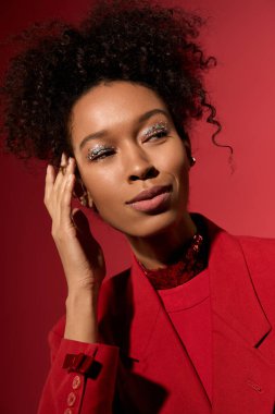 Genç bir kadın, kendine güveni yumuşak bir gülümseme ile koyu kırmızı bir arka plana karşı, güzelliği ön plana çıkarıyor..