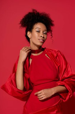 Çarpıcı kırmızı kıyafetli güzel genç bir kadın renkli bir ortamda neşe ve kendine güveni ifade ediyor.