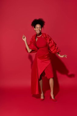 Kırmızı elbiseli güzel bir kadın cesur kırmızı bir ortamda şakacı bir şekilde dans ediyor..