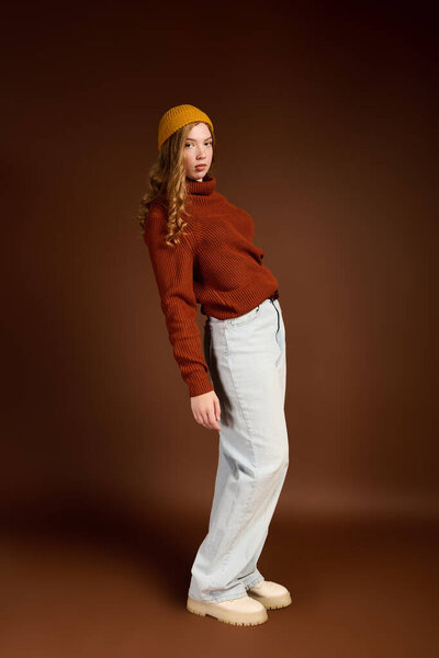 Young woman with lovely red hair poses in a cozy winter sweater against a warm brown background.