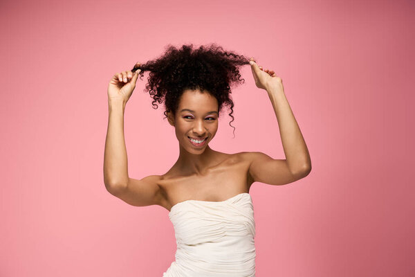 A beautiful young woman with curly hair smiles radiantly while playfully tugging at her curls.
