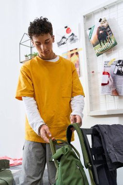 Genç çocuk sırt çantasını düzenliyor, hareketli ve canlı bir odada şık bir kıyafet sergiliyor..