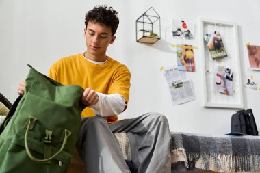 Günlük kıyafetli genç bir çocuk yeşil bir çantayla evde rahat bir atmosfer yaratıyor..