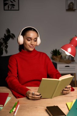 Genç bir Afrikalı Amerikalı kadın şık dairesinde sessiz bir akşam okumanın keyfini çıkarıyor..