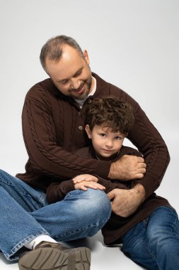 Neşeli bir sahne oğlunu kucaklayan bir babanın samimi evinde sevgisini ve kahkahasını paylaştığını gösteriyor..