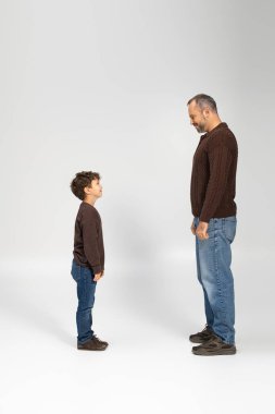 Baba ve oğul birlikte durur, gülüşlerini ve mutluluklarını rahat kahverengi kazaklarıyla paylaşırlar..