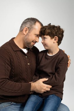 Bir baba ve küçük oğlu yan yana oturur, sırıtışlarını ve sıcaklıklarını paylaşırlar..