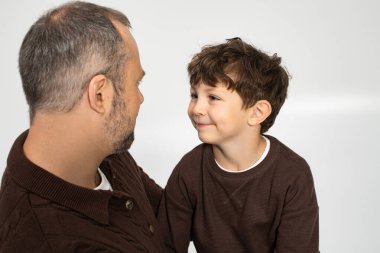 Bir adam, sıcak bir ortamda mutlu bir şekilde gülümseyen küçük oğluyla hassas bir anı paylaşır..