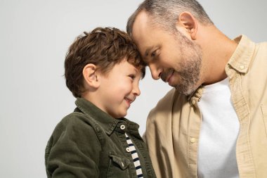 Bir baba ve oğlu neşe dolu, şefkatli bir anı paylaşıyor, gülümsemelerle yakınlaşıyorlar..