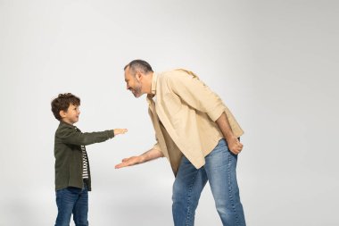 Bir baba ve küçük oğlu neşeyle etkileşime girer, parlak bir odada neşeli bir jest paylaşırlar..