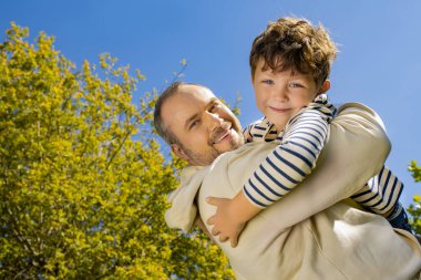 Neşeli bir baba, canlı bir sonbahar manzarasıyla çevrili küçük oğluna sarılır..