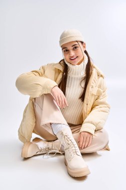 Modayı takip eden genç bir kız, parlak beyaz bir stüdyoda poz verirken kışlık kıyafetini sergiliyor..