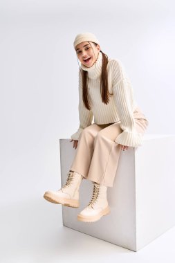 Pretty teenager dressed in a cozy winter outfit poses happily in a bright studio.