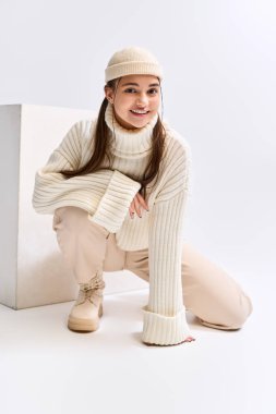 Neşeli bir genç kız şık bir kış elbisesi içinde poz verir, parlak bir stüdyoda sıcaklık saçar..