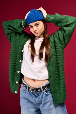 Mavi bereli ve yeşil hırkalı kız kırmızı bir arka plana karşı gençlik modasını ifade ediyor..