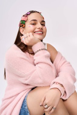 Renkli saç tokaları ve parıltılarla süslenmiş pembe hırkayla gülümseyen şık bir genç kız..