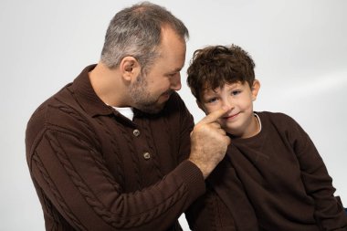 Sevgi dolu bir baba, oğlunun burnuna neşeyle dokunurken gülümser. Yürek ısıtan bir sahne yaratır..