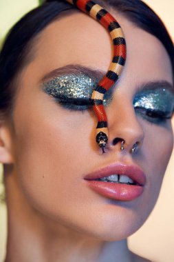 Güzel genç bir kadın renkli bir yılanla cesurca poz verir. Zarafet ve tehlike gösterir..