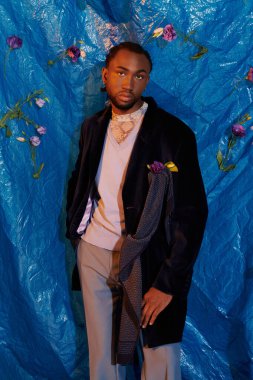 Şık bir genç adam, modaya uygun kıyafetiyle canlı bir mavi zemine karşı güvenle poz verir..