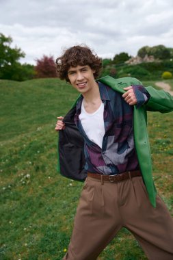 Genç adam dışarıda neşeli bir yürüyüş yapıyor, gülümsüyor ve doğanın hoş atmosferini kucaklıyor..