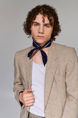 Şık bir ceket ve eşarp giyen kendine güvenen genç, sade bir arkaplana karşı aktif bir poz veriyor..