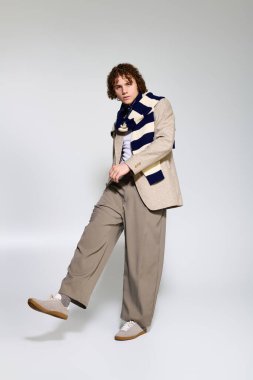 Moda kıyafetleri giyen genç, tarafsız bir arkaplana karşı enerjik bir poz verdi.