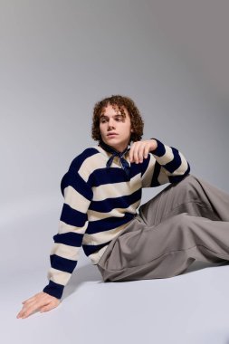 Genç, modaya uygun kıyafetlerle poz veriyor. Sanatsal stüdyo alanında rahat ama enerjik bir hava var..