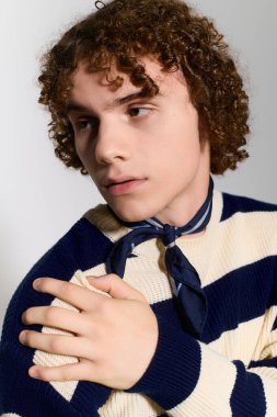 Kıvırcık saçlı bir genç evde dinamik bir poz verirken çarpıcı bir kıyafet giyiyor..