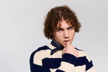 Kıvırcık saçlı genç stüdyo ışıklarında şakacı poz verirken modern moda sergiliyor..