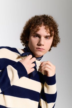 Kıvırcık saçlı ergen, aktif pozlar veriyor ve iç mekanda şık bir kıyafet giyiyor..