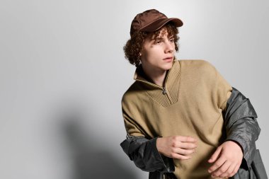 Kıvırcık saçlı ve şık kıyafetli bir genç, gösterişli bir arkaplanda rahatça poz veriyor..