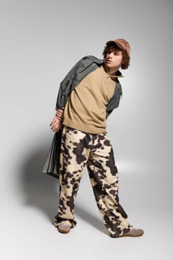 Moda kıyafetli genç, basit bir arka plana karşı aktif bir duruş sergiliyor..