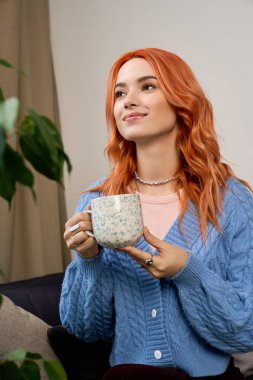 Kızıl saçlı genç bir kadın rahat bir şekilde evinde oturuyor, sıcak bir içkinin keyfini çıkarıyor..