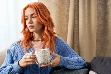 Kızıl saçlı genç bir kadın evinde çayını yudumlarken rahat bir şekilde dinleniyor..
