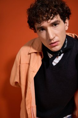 Genç bir adam cesur turuncu bir arka plana karşı şık katmanlar halinde poz verir..