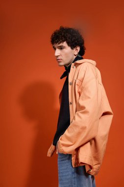 Moda kıyafetleri içinde yakışıklı bir adam cesur renklerle dolu sanatsal bir ortamda rahatça poz veriyor..