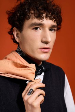 Şık bir adam moda anlayışını açık bir eşarpla, koyu turuncu bir arka planda sergiliyor..