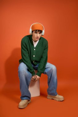 Şık bir genç adam kendine güvenerek oturur, modern modayı göstererek yeteneklerini ve cazibesini sergiler..