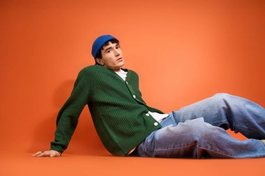 Yakışıklı bir adam parlak turuncu bir arka planda, kendine has moda anlayışını sergiliyor..