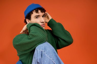 Yakışıklı bir adam moda tarzını örgü yeşil kazak ve mavi şapkayla sergiliyor..