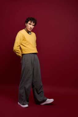 A fashionable man stands confidently, wearing a bright yellow top and sleek trousers, exuding charm.