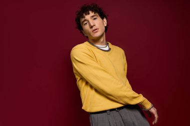 Yakışıklı şahıs, koyu bir bordo duvarın önünde son moda sarı bir kazak sergiliyor..